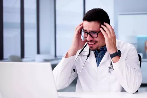 Fejét fogó orvos néz a monitorra