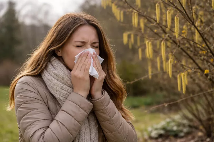 Allergiás nő mogyoróbokorral a háttérben.