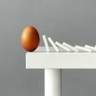 Asztal szélén kiegyensúlyozott tojás felé dőlő dominók